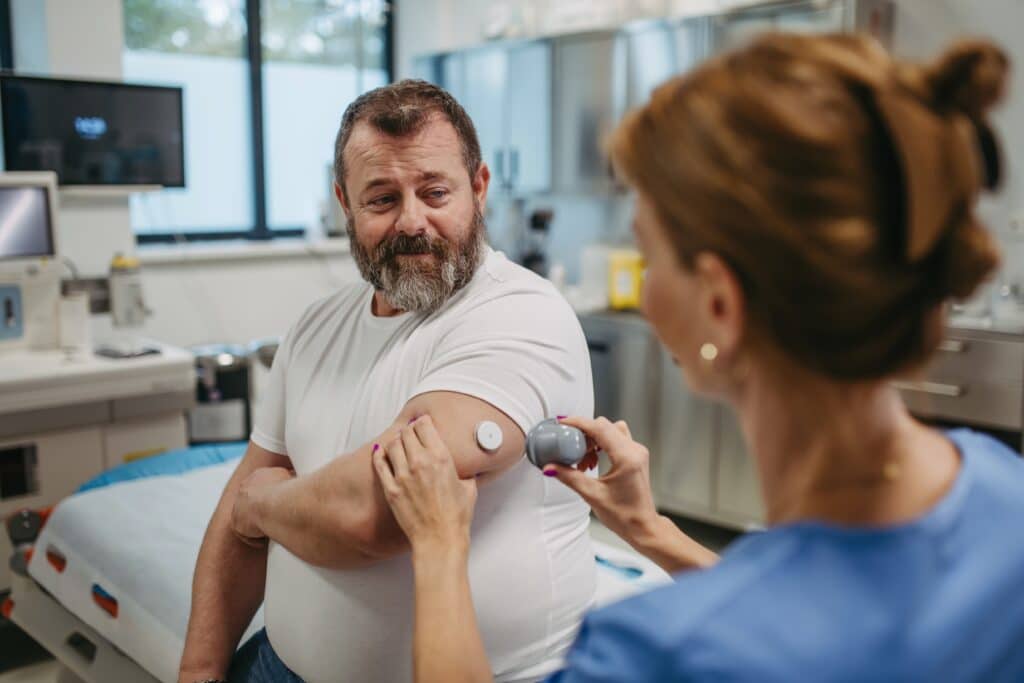 Man having his glucose monitor attached by a doctor to manage his diabetes