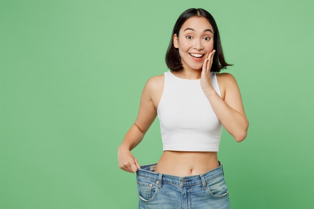 A woman smiling and holding her jeans away from her waist after using tirzepatide for weight loss