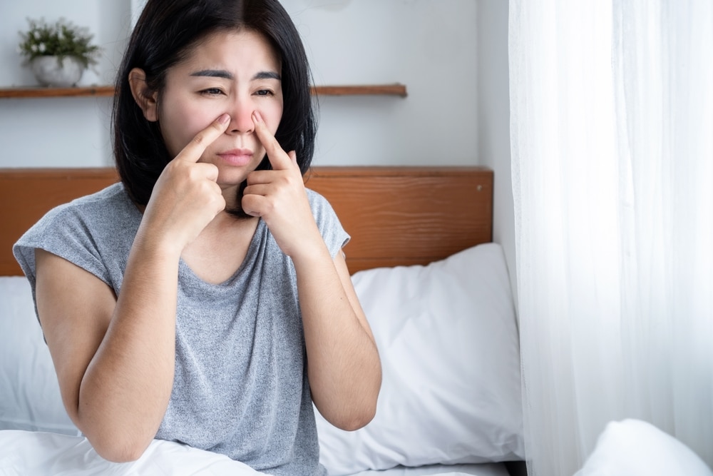 A woman with allergies sitting in bed and touching her nose