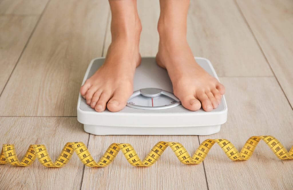 A close-up shot of a person standing on a scale with a tape measure on the floor