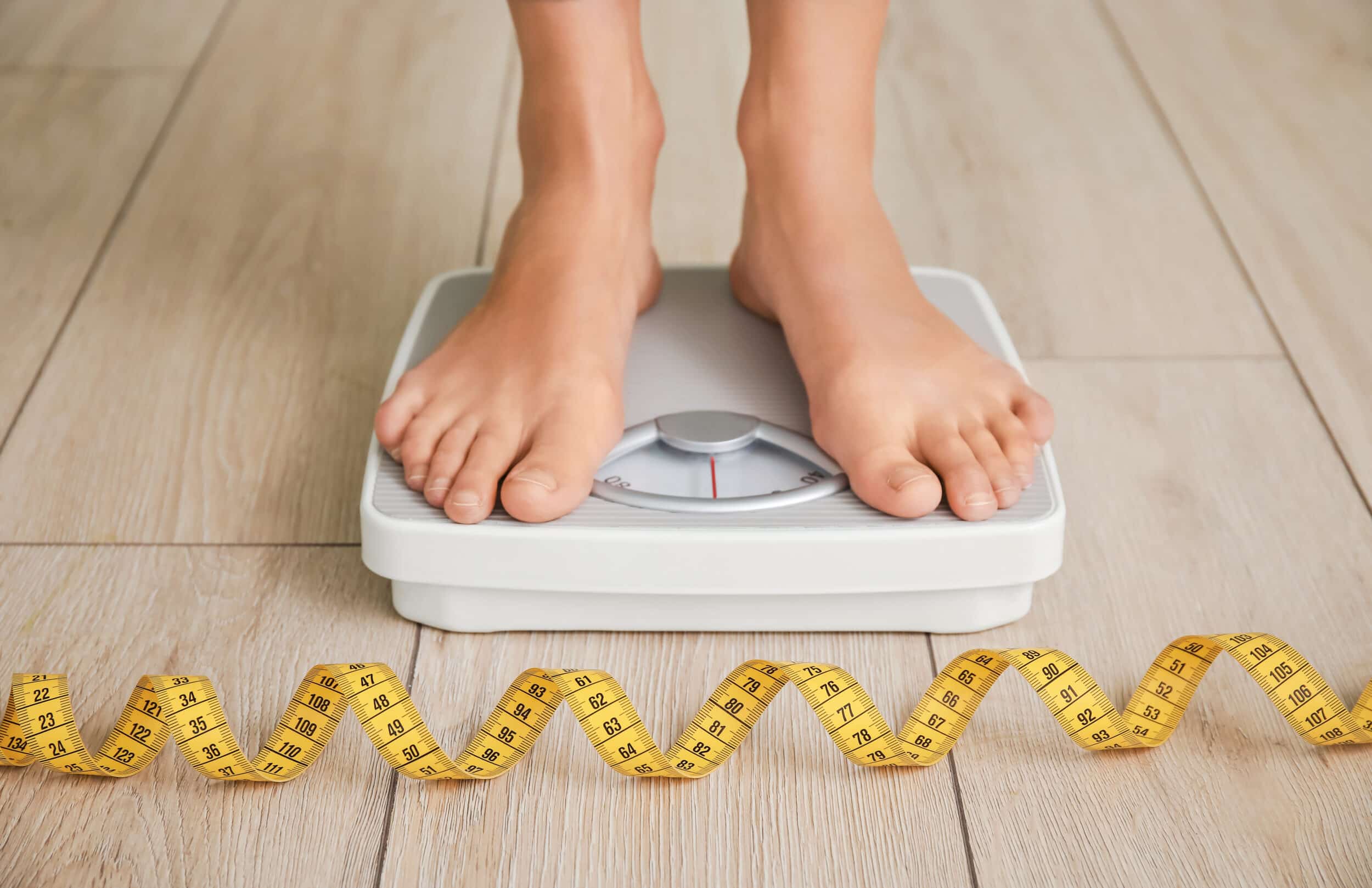 A close-up shot of a person standing on a scale with a tape measure on the floor
