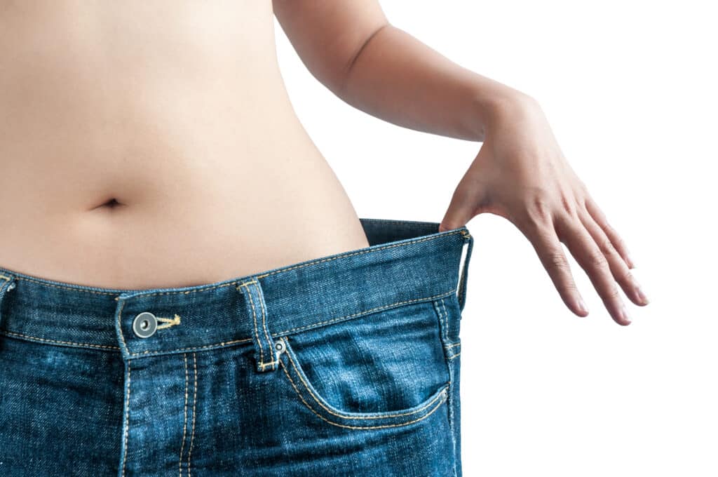 A cropped shot of a woman on tirzepatide holding her jeans away from her waist