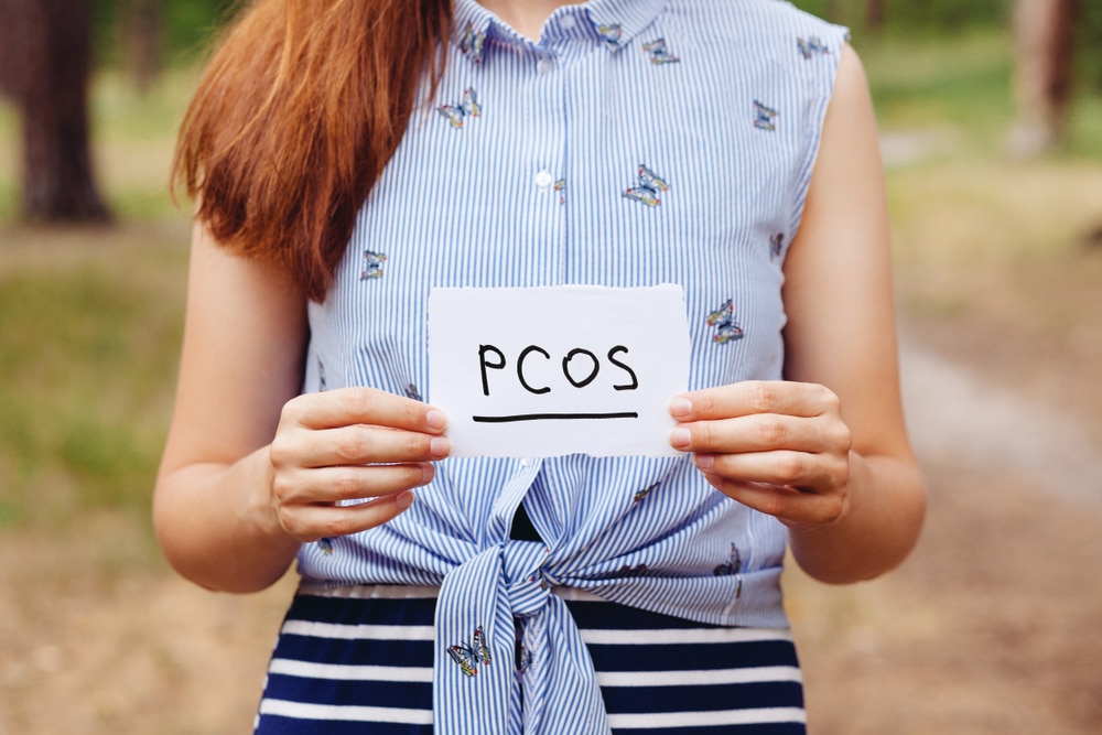 A woman holding a card that says “PCOS”