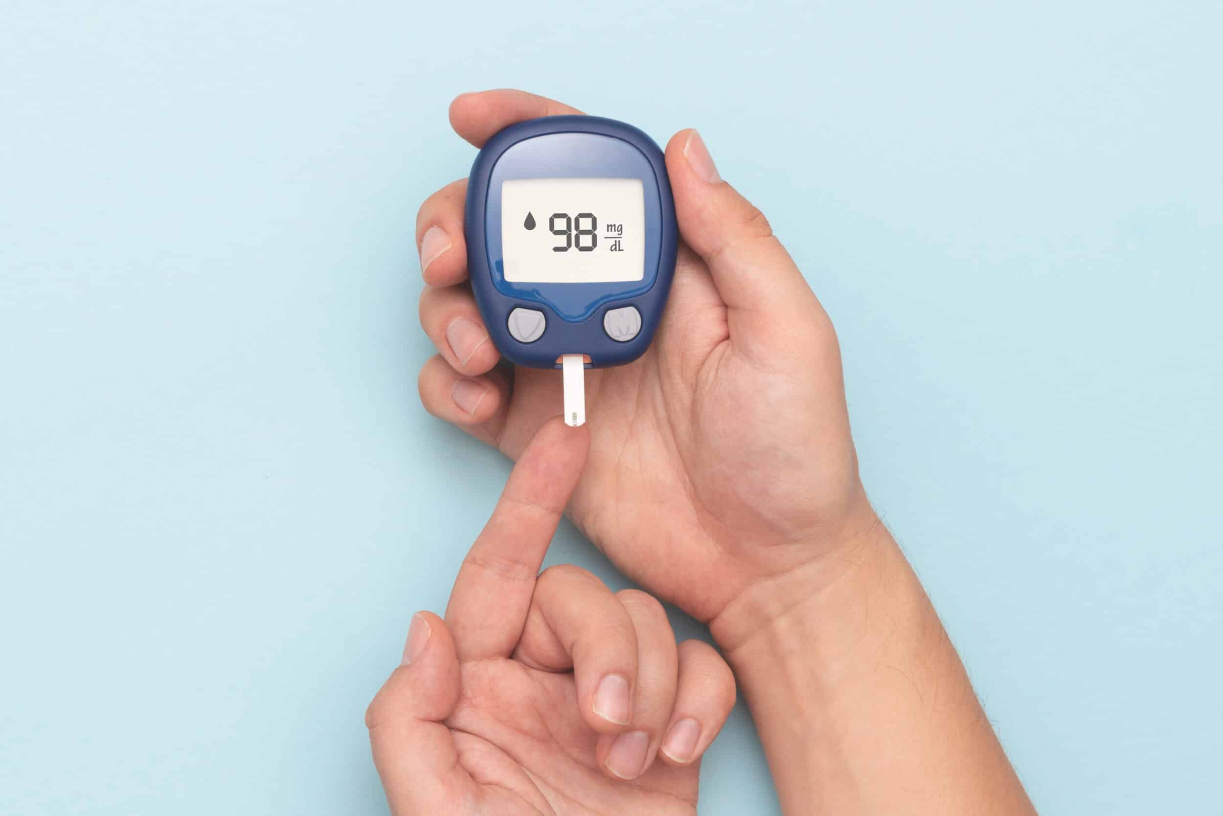 Man using glucometer, checking blood sugar level. Diabetes concept on blue background