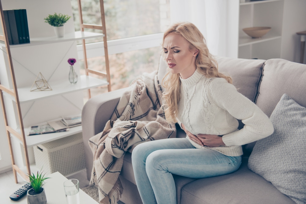 A woman with a stomach ulcer sitting on a couch, holding her abdomen