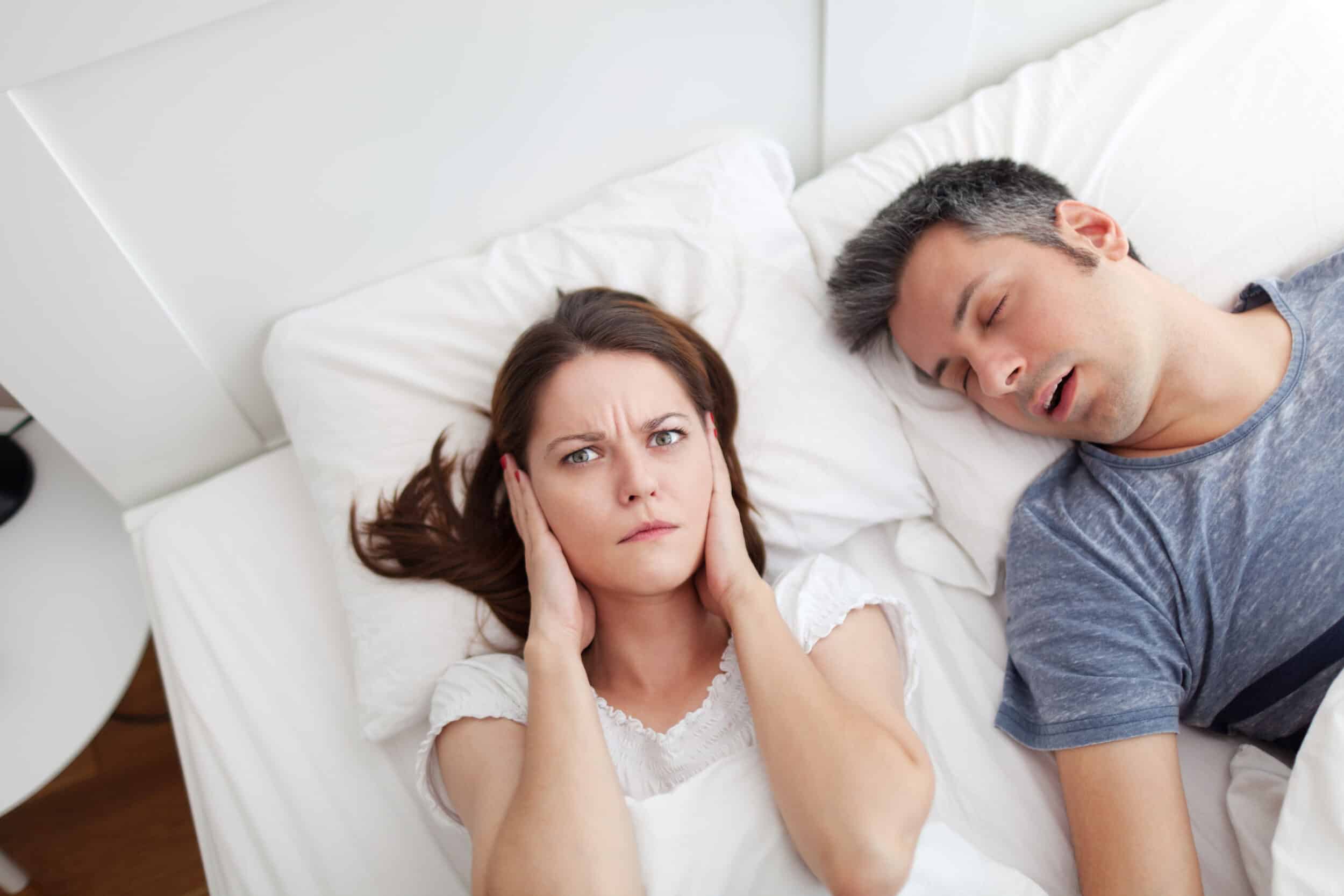 A woman covering her ears while her husband with sleep apnea snores A woman covering her ears while her husband with sleep apnea snores