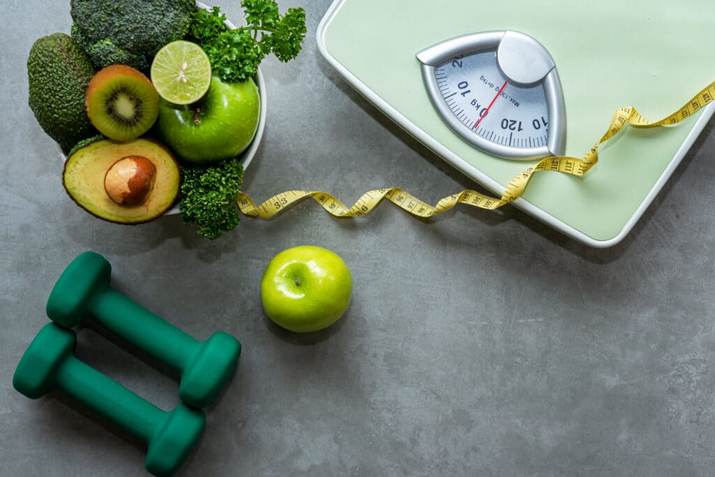 Person standing on scale, interested in semaglutide treatment for weight loss. Scale, dumbbells, tape measure, and bowl of fruit